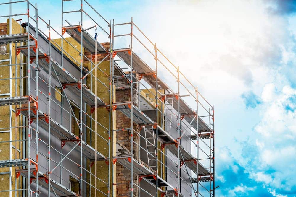 Commercial building exterior under construction with metal scaffolding, insulation material, and new siding panels for a tenant improvement project.